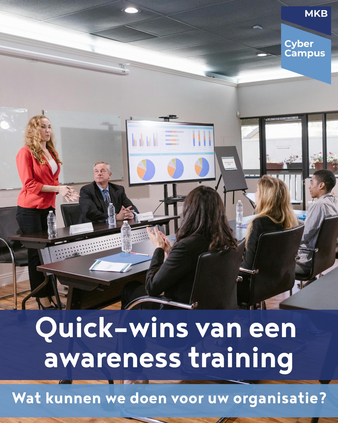 "Groepsfoto van een awareness training van MKB Cyber Campus: een trainer staat voor een groep deelnemers in een vergaderruimte en legt uit hoe cybersecurity werkt, met een scherm met grafieken en statistieken op de achtergrond."